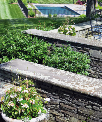 Intricate stone walls with accompanying plantings leading down to a landscaped pool area.
